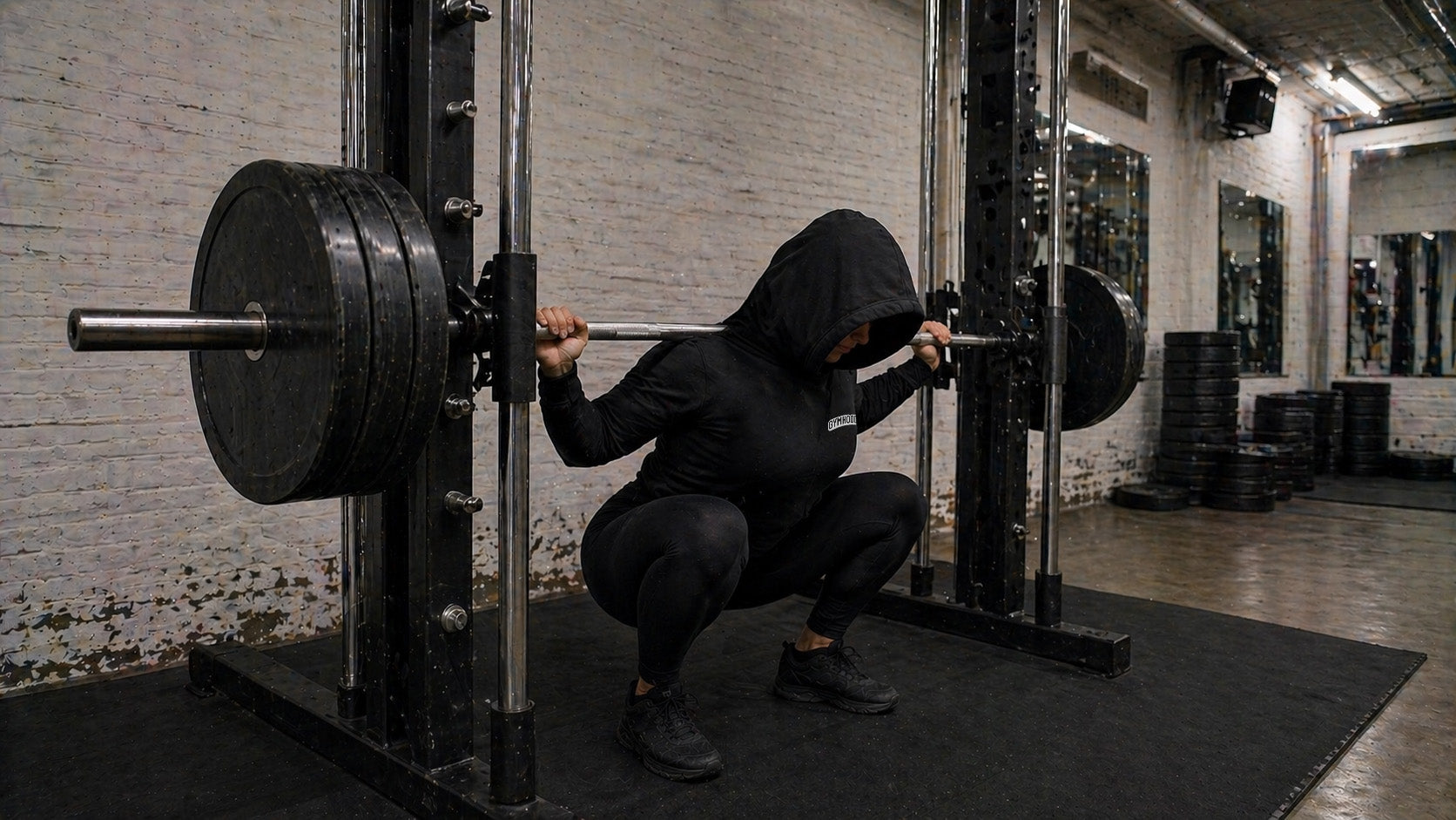 Strong female lifter at the bottom of a Smith machine squat, GYMHOOD hoodie
