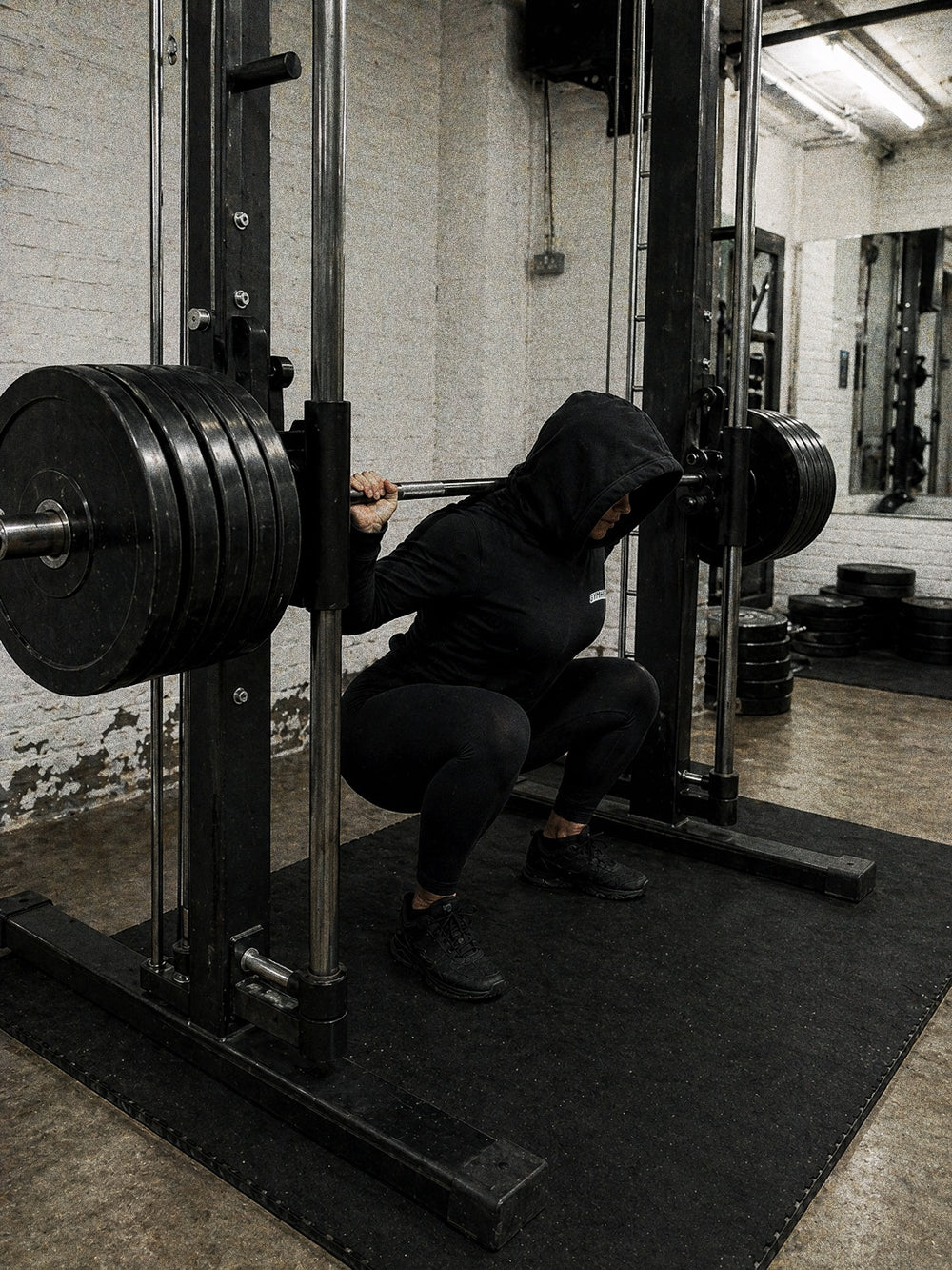 Strong female lifter at the bottom of a Smith machine squat, GYMHOOD hoodie