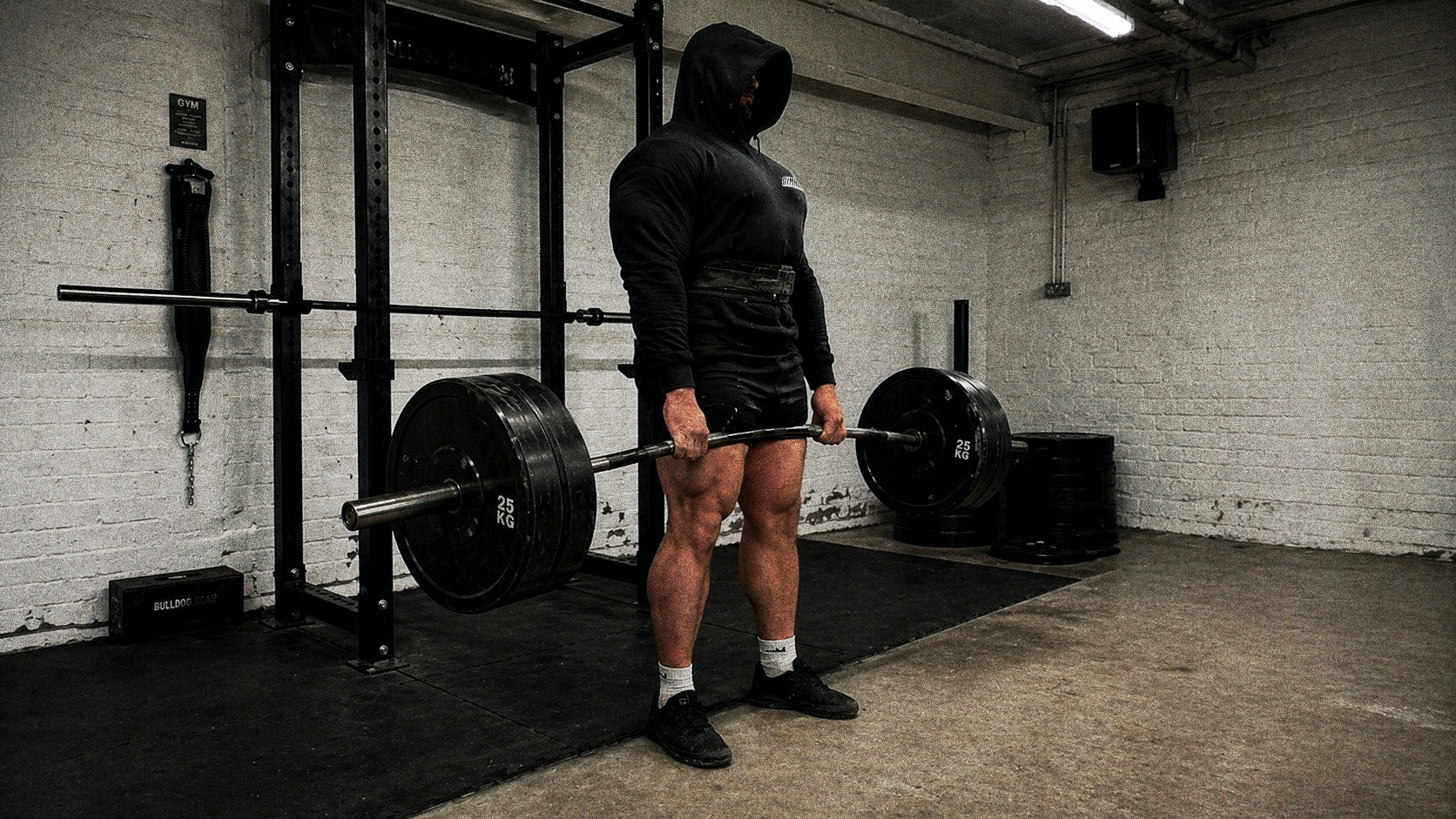 Hooded GYMHOOD lifter at the top of a heavy deadlift lockout in a real UK gym