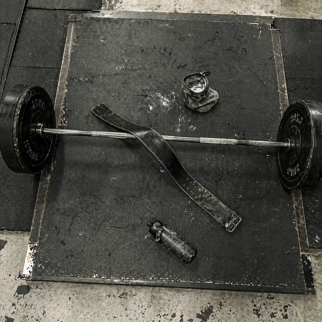 Loaded barbell, lifting belt, chalk and water bottle on a worn lifting platform