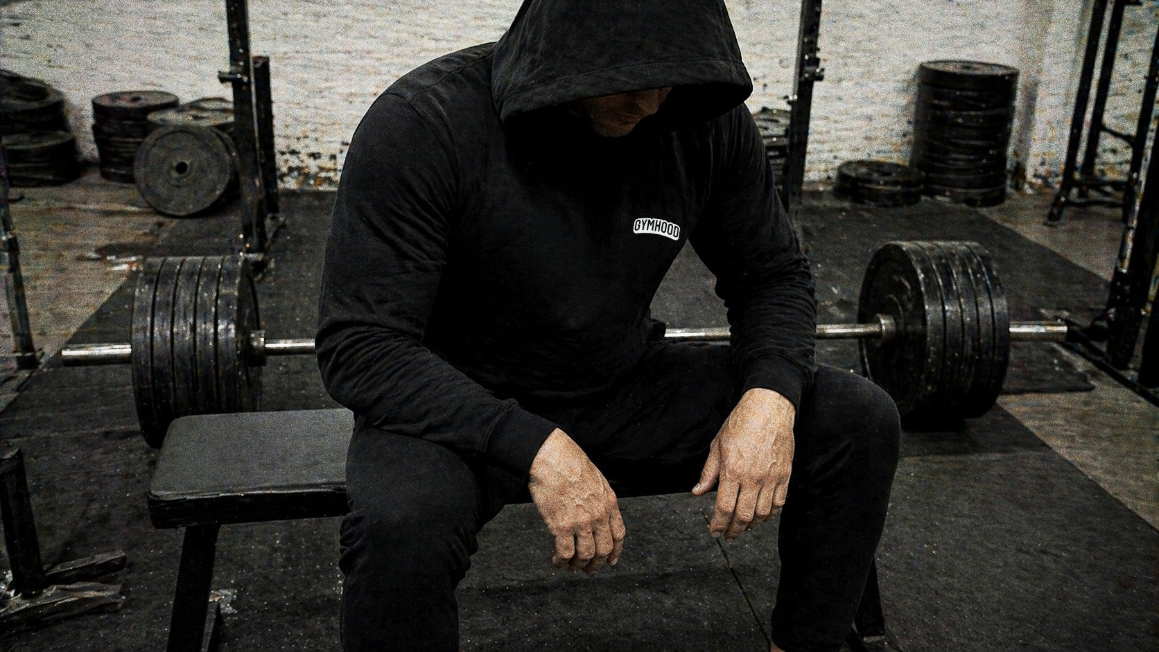 Hooded lifter resting on a bench between sets in a working UK gym
