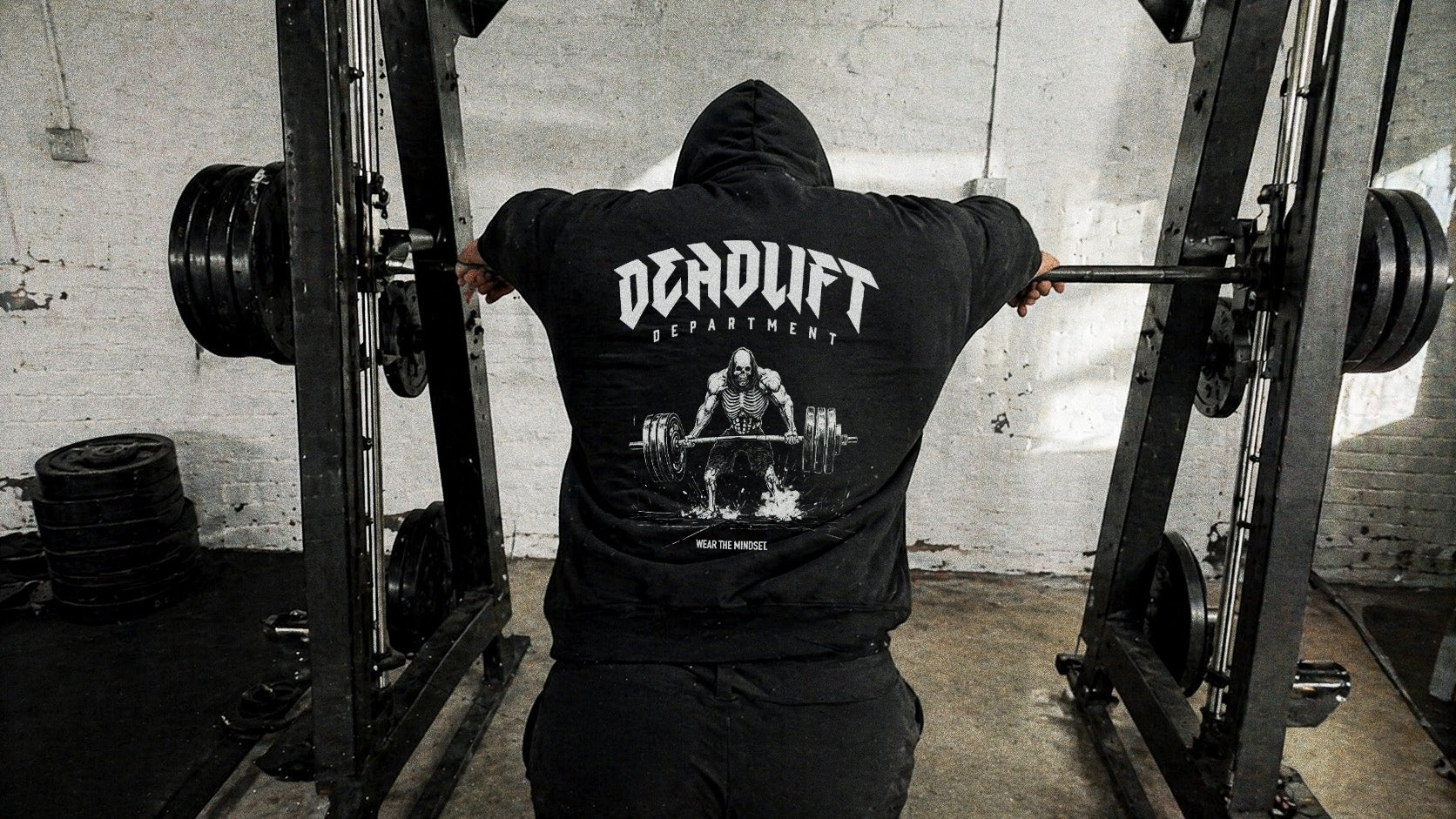 Hooded lifter leaning on a Smith machine after a heavy set, GYMHOOD hoodie